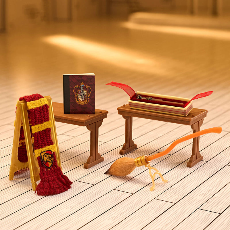 Miniature wooden table with books, a broomstick, and a scarf on a wooden floor.