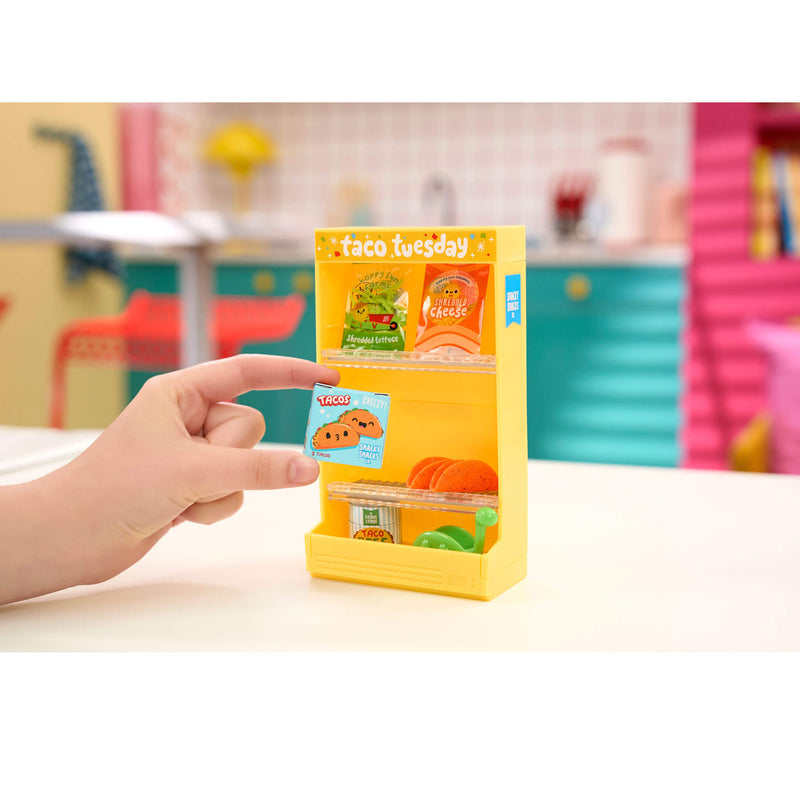 Hand holding a yellow packaging box with 'taco tuesday' branding on a blurred indoor background.