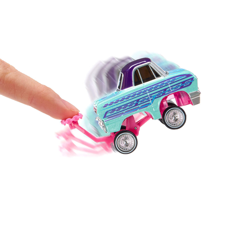 A small toy car with a blue body is being pushed by a human finger on a white background, with motion blur effects around the car and pink trail.