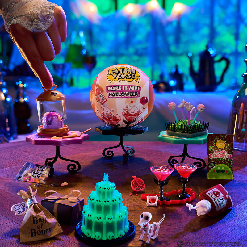 A tabletop display of a mini Halloween items set under colorful neon lighting. A hand is visible at the top left touching one of the small accessories.