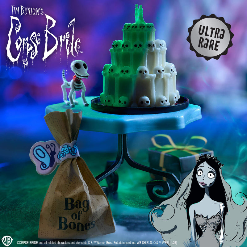 A Tim Burton's Corpse Bride themed collectible display featuring a green and white ghost cake on a pedestal stand, a small skeleton figurine, a brown paper bag labeled 'Bag of Bones,' and character artwork. Visible text includes 'Tim Burton's Corpse Bride,' 'ULTRA RARE,' and copyright credits for Warner Bros.