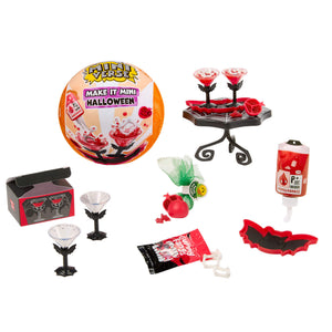 Halloween mini craft kit with a round orange ball labeled 'Make It Mini Halloween' and various small accessories including black stemware, red roses, a small stand, fake blood, a bat-shaped piece, and other themed pieces on a white background.