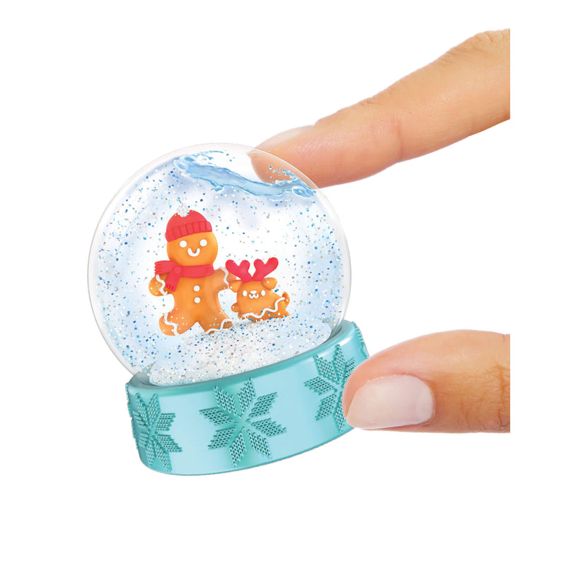 Two fingers holding a mini snow globe with a gingerbread man and pet inside on a white background
