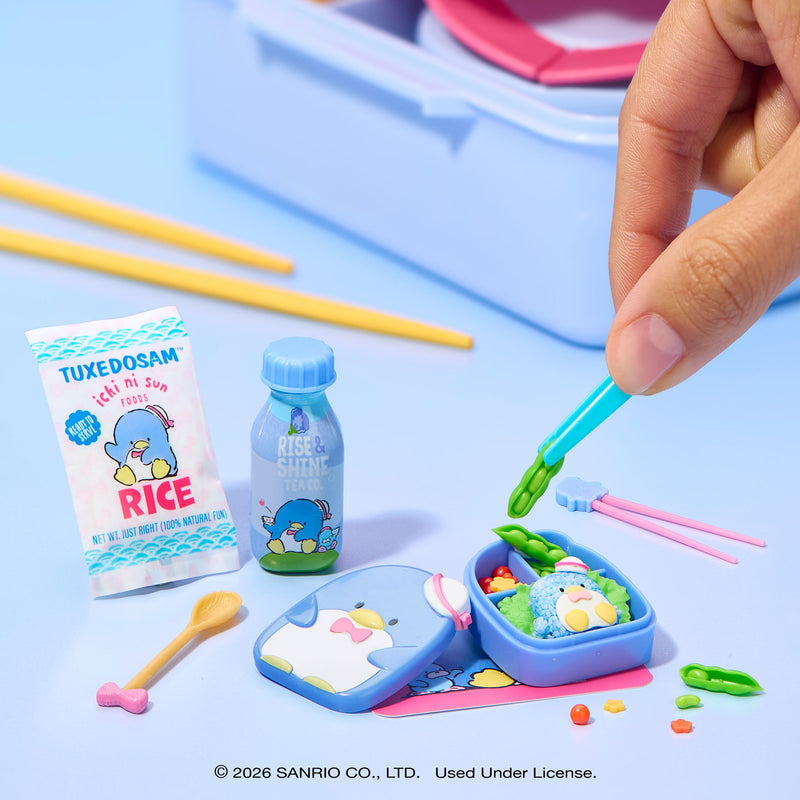 Blue penguin-themed bento box with compartments and a pair of pink chopsticks adding food on a blue background.