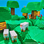 A Minecraft-themed scene built from green blocky hills, trees, and sheep, with a bee, beehive, flowers, and a small figure in the background. The scene is photographed against a bright blue backdrop.