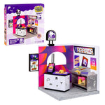 Miniverse Taco Bell branded set and its packaging. Packaging details include a circular badge “30+ PIECES,” age indicator “8+” and text “1 SET / ENSEMBLE.”  Shows a small a white tile-patterned service counter with black top and small doodle-style icons (taco, Taco Bell bell, “TACOS”) with bright Taco Bell branding and colorful purple/orange gradient graphics.