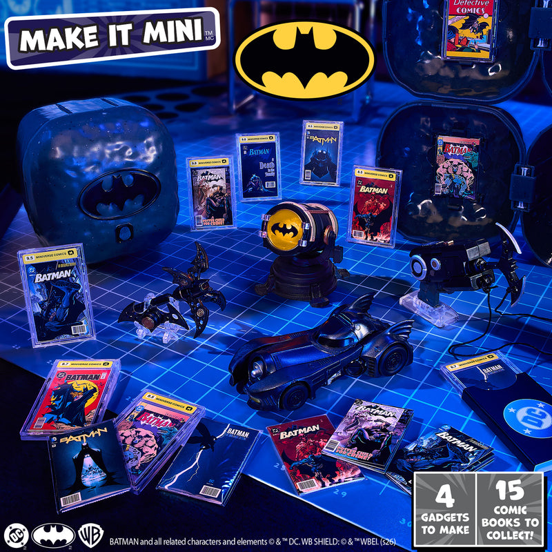 A Batman-themed mini toy and collectible display arranged on a blue grid surface, including a bat-shaped car, comic books, a Bat-light prop, and a purple Batman-themed  case.