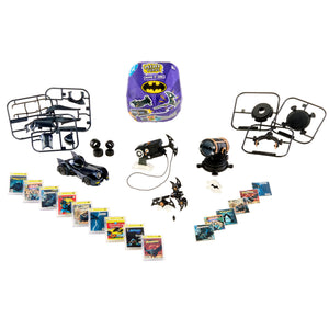 A Batman-themed mini toy set laid out on a white background, including a small black RC car, two black RC drones with frames, a purple Batman-branded storage box, several small accessory pieces, and multiple comic book cards or inserts arranged in rows.