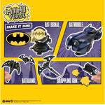 A comic-style product display card for a Batman Mini Verse toy set on a bright yellow background. The card shows several small Batman-themed accessories labeled 'Bat-Signal,' 'Batmobile,' 'Batarang,' and 'Grappling Gun,' along with hands holding some pieces.