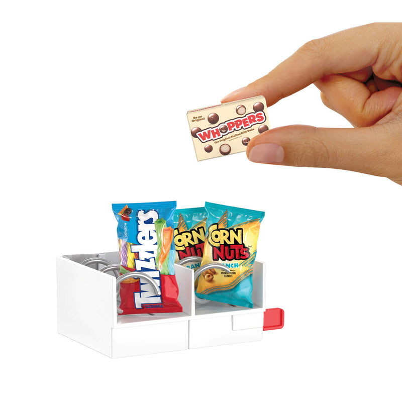 Hand holding a miniature Whoppers candy bar with a display of other miniature snack packages on a white background.