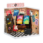 Miniature record store display with vinyl records, guitar, and amplifier against a brick wall.