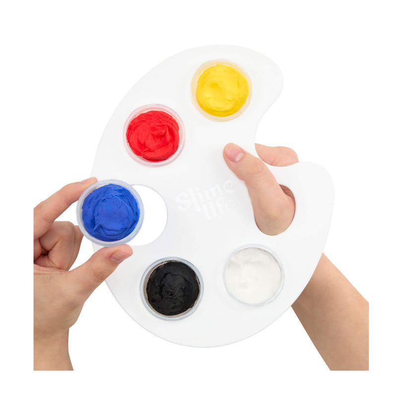 A white artist palette with five wells containing yellow, red, blue, black, and white substances, held by two hands against a white background.