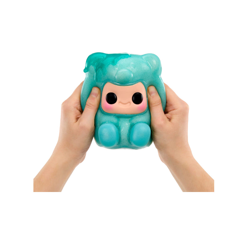 Hands-holding and squishing a Blue Gummy Bear, featuring a cute cartoon face on the front, with blue feet, shown against a plain white background.