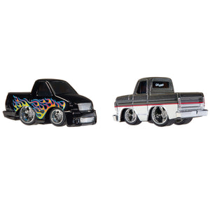 Two die-cast toy pickup trucks on a plain white background. The left truck is black with colorful flame decals in blue, yellow, orange, and red.