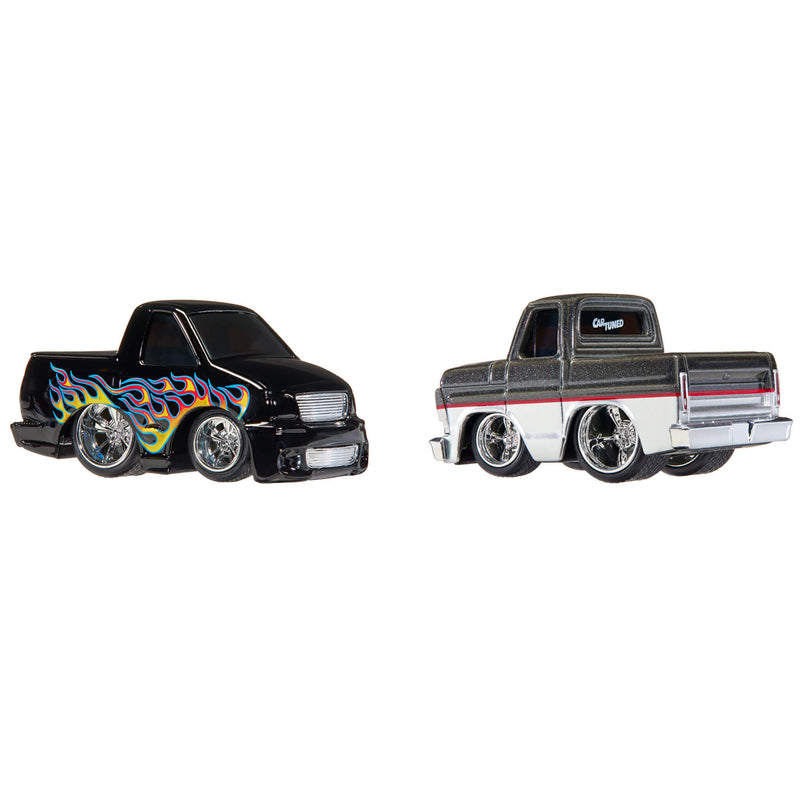 Two die-cast toy pickup trucks on a plain white background. The left truck is black with colorful flame decals in blue, yellow, orange, and red.