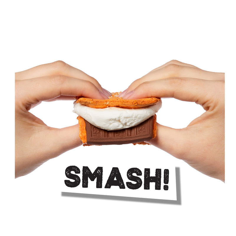 Two hands smash a smores style novelty item, white marshmallow-like material, and a brown chocolate bar-shaped center, with the word "SMASH!" below on a white background.