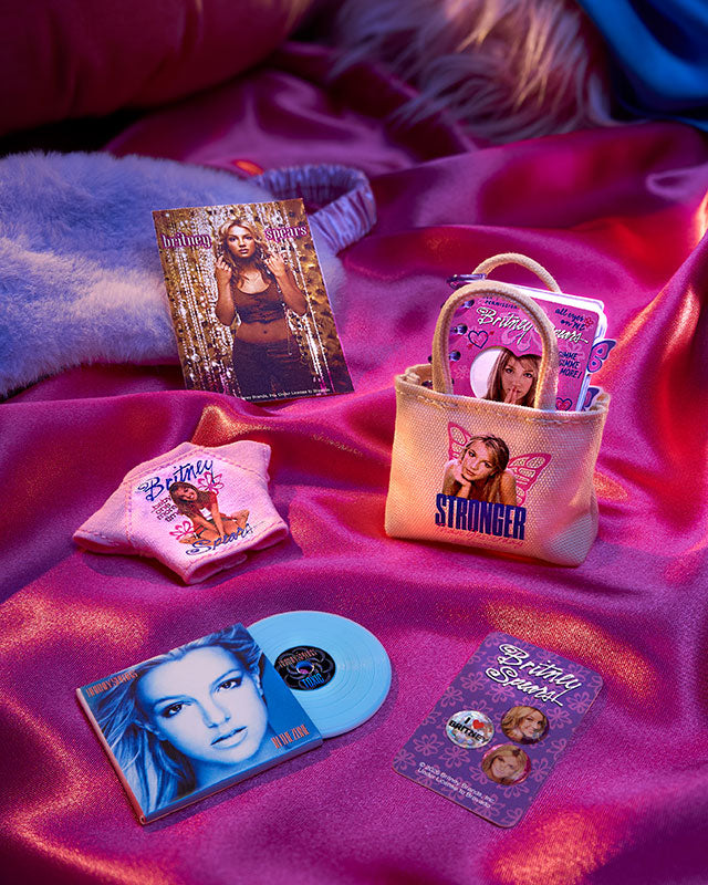 Collection of MGA's Miniverse Real Music Britney Spears Special Edition including a tote bag, t-shirt, and vinyl record on a pink fabric background.
