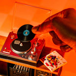 Person placing a mini vinyl record on a mini turntable with an orange background