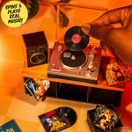 Person placing a mini vinyl record on a mini turntable with a warm orange glow.