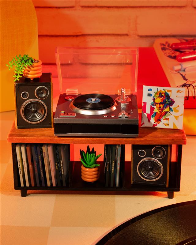 Miniverse Miniature record player with speakers and vinyl records on a table with a 'Your Local Record Shop' sign in the background.