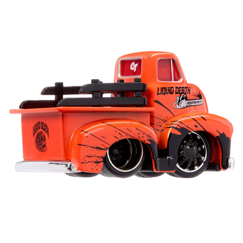 A die-cast toy model of a vintage pickup truck in bright orange with black splatter graphics, black tires, and 'Liquid Death' branding on the side and bed.