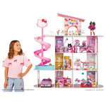 A Hello Kitty dollhouse playset with a pink spiral slide, a cat-themed upper room, and multiple dollhouses and accessories displayed inside, shown next to a young girl wearing a pink Hello Kitty t-shirt.