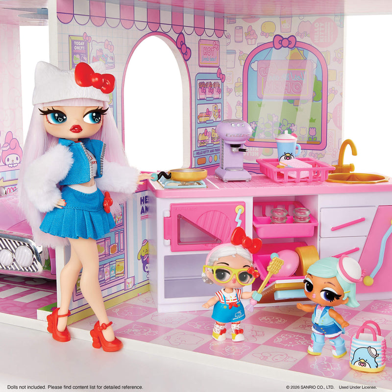 A doll playset featuring a large fashion doll with long white hair, a white cat-ear hat with a red bow, and a blue outfit, standing beside a pink bakery play kitchen with two smaller dolls. The set includes miniature appliances, a sink, and storage cabinets.