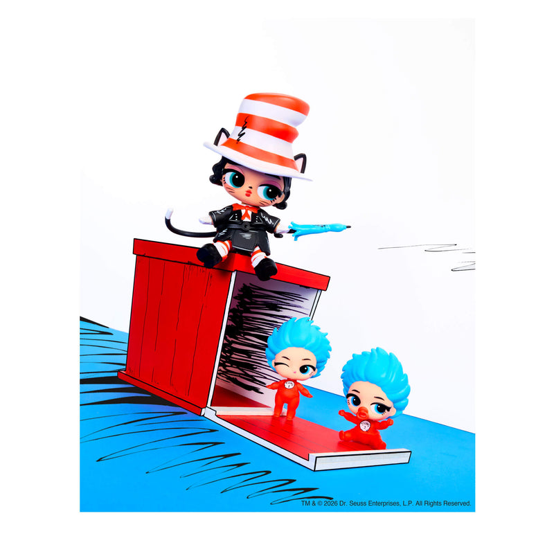 This is a brightly colored staged photo of three stylized toy figures and a small red box/door prop, photographed against a white background with a blue floor area. A cat-like toy sitting on top of the red box and two small like figures with bright blue hair, on the open red lid.