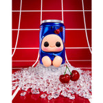 A blue cartoon character figurine soda can, surrounded by scattered clear ice cubes and two red cherries on a glossy red surface, with a red background featuring white grid lines.