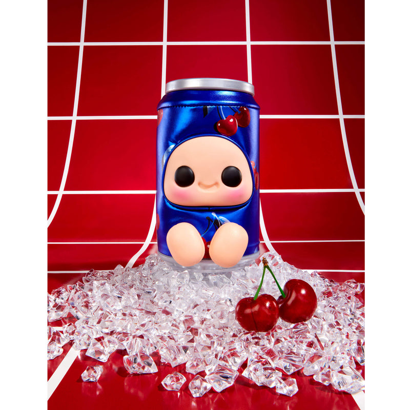 A blue cartoon character figurine soda can, surrounded by scattered clear ice cubes and two red cherries on a glossy red surface, with a red background featuring white grid lines.