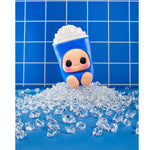 A blue character-shaped toy cup with a smiling face, emerging from a pile of clear ice cubes on a blue surface against a blue tiled background.
