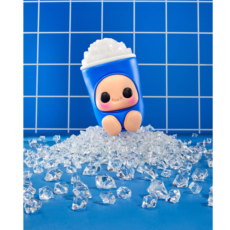 A blue character-shaped toy cup with a smiling face, emerging from a pile of clear ice cubes on a blue surface against a blue tiled background.