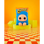 A Cheetos-themed plush toy shaped like a blue snack bag with a cartoon face, displayed on a yellow pedestal against a bright orange background with geometric blocks and a checkered floor.