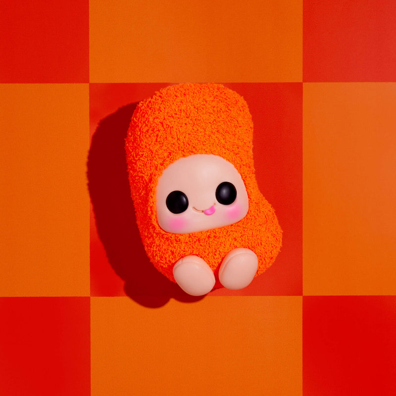 A small orange fuzzy plush toy with a pale face, large black eyes, and pink cheeks sits centered on a bold orange and red checkered background.