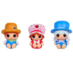 Three small doll figures with large black eyes are shown side by side on a plain white background. The left doll wears a brown hat and blue outfit with green accents.

