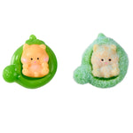 Two small plush toy figures on a plain white background: one sitting upright in a green leaf-like holder and one curled up inside a fuzzy green leaf-shaped wrap. Both figures have pale peach faces and bodies that are cream-colored.