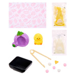 A cute food-themed craft playset featuring a pink patterned mat, a purple shaped cave with green leaves, a small yellow chick figure, a black tray, wooden tongs, and several small food-shaped beads and accessories, all arranged on a white background.