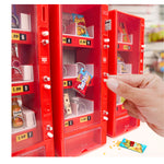 Three red mini vending machines shown side by side on a white table, with a hand pushing a button to get some Twizzlers.