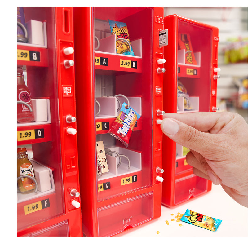 Three red mini vending machines shown side by side on a white table, with a hand pushing a button to get some Twizzlers.