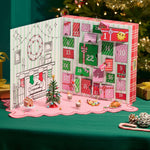 Miniverse Make it Mini Holiday packaging open to show numbers one through twenty-four, on the left side is a fireplace with stockings, a wreath on a green and white striped background. Various mini’s sitting in front of the open packaging on a green table cloth.