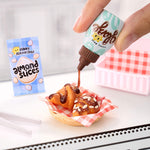 Hand drizzling mini chocolate sauce onto a pastry with a Sunny Seasonings almond slices packet in the background.
