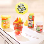 Mini fruit salad in a glass with colorful containers labeled 'Sweet & Tangy' and 'Mango Soft Serve' on a kitchen counter.