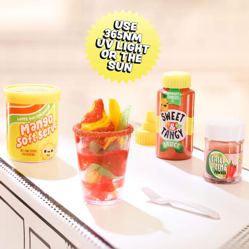 Mini fruit salad in a glass with colorful containers labeled 'Sweet & Tangy' and 'Mango Soft Serve' on a kitchen counter.