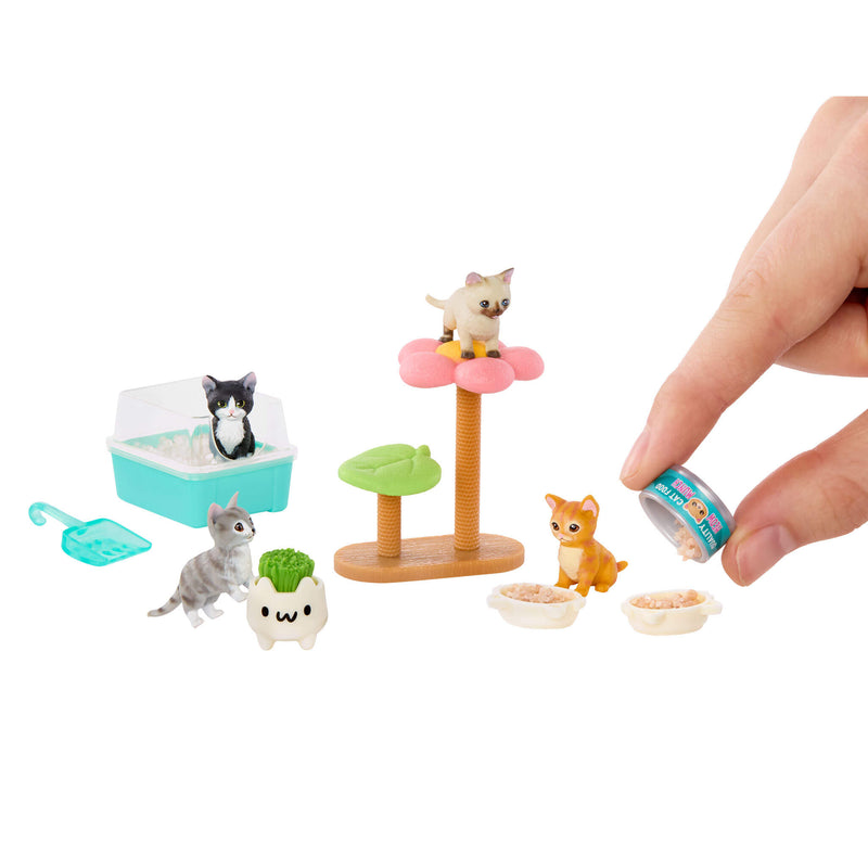 A miniature pet set with small cat figurines, a flower-shaped cat tree, bowls, a litter box, and a toy scoop, shown on a white background with a human hand holding a tiny can.