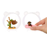 Two small animal-themed miniature display cases on a white background, one containing a sloth figure and one being held by a hand containing a dachshund figure. A pink bed-like accessory is visible inside the right case.