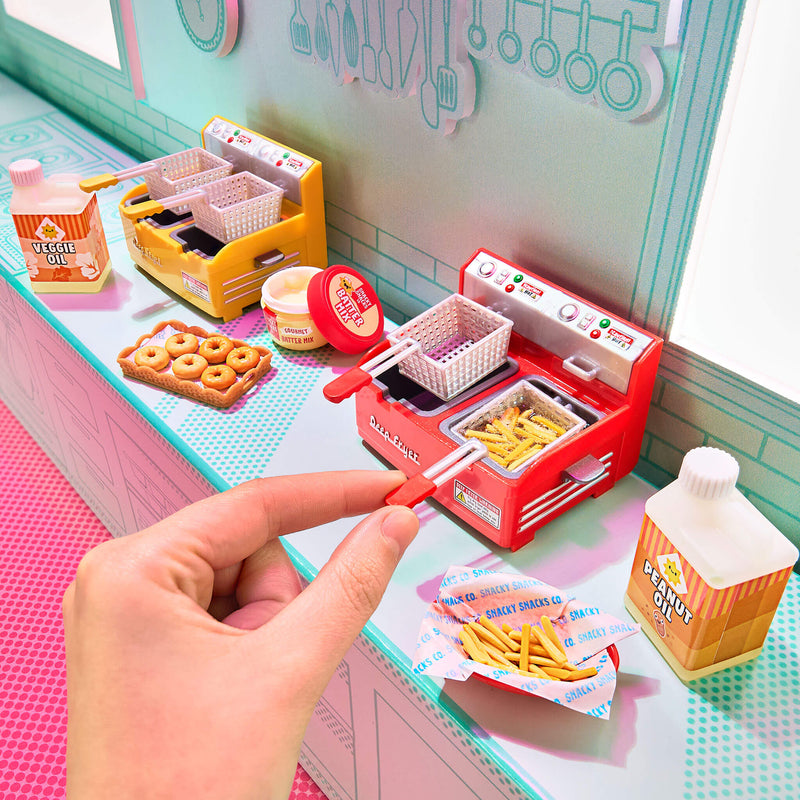 Miniature food setup with a hand holding a fryer basket of fries on a colorful surface.