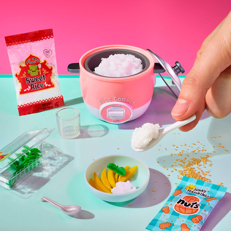 Pink rice cooker with a hand scooping rice, surrounded by snacks and a bowl of fruit on a colorful background.