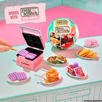 Miniature waffle maker set with waffles and other food items on a pink and blue surface.