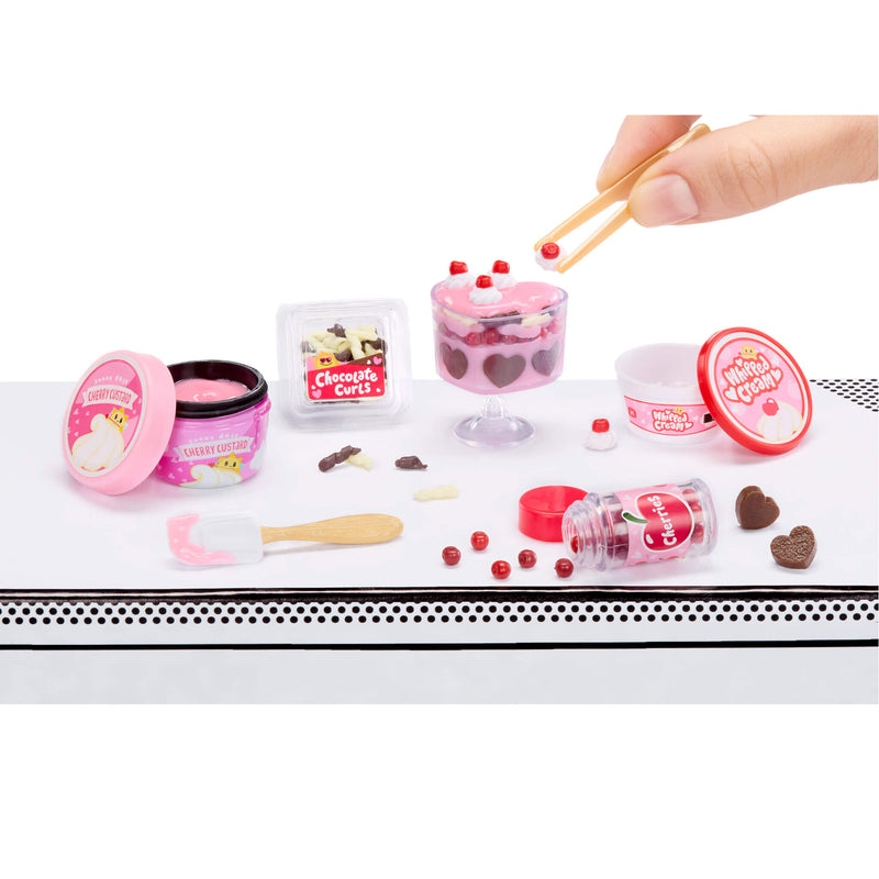 Miniature trifle set with a hand using tweezers on a white surface