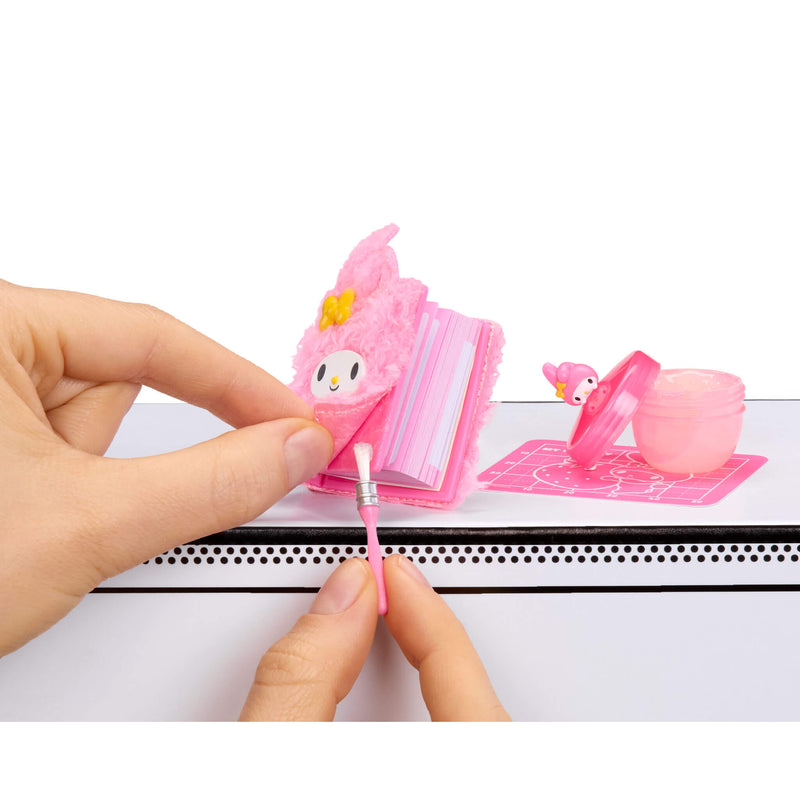 Hand holding a pink brush with a Hello Kitty character design on a book with a white background